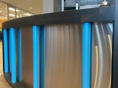 Curved reception desk front facade - brushed stainless steel privacy paenl with ebony stained pine top and base and branded blue pipe
