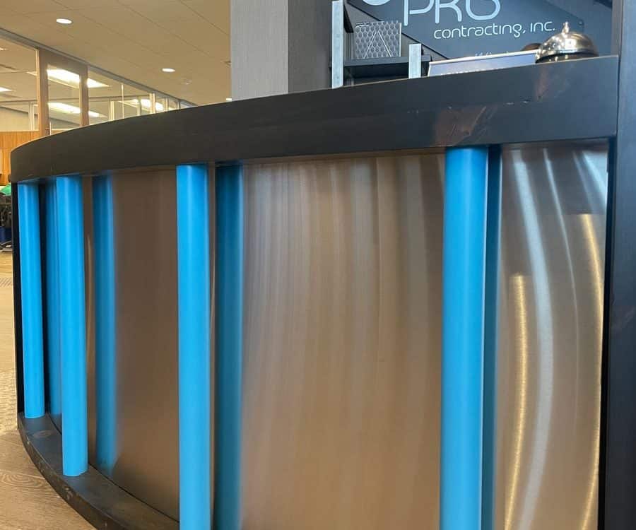 Curved reception desk front facade - brushed stainless steel privacy paenl with ebony stained pine top and base and branded blue pipe