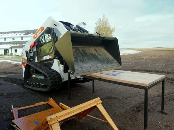 Skid steer lifting itself up off of Grain Designs dining table